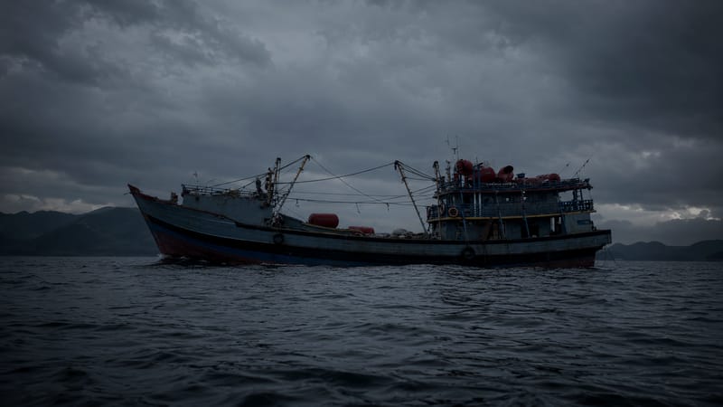 A traditional fishing vessel on calm water under a moody dusk sky.